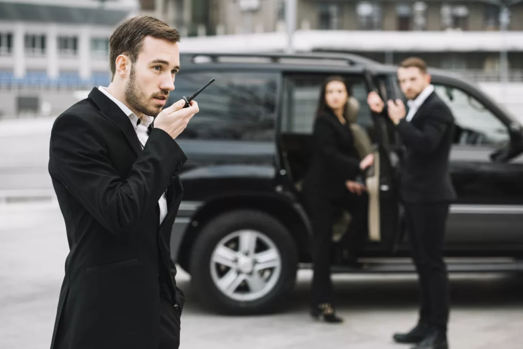 Security professionals in suits coordinate with walkie-talkies as they escort a client into a black SUV, illustrating vip security services by HK Defense Solutions.