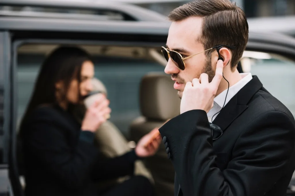 Professional bodyguard in a black suit and sunglasses protecting an executive woman exiting a vehicle
