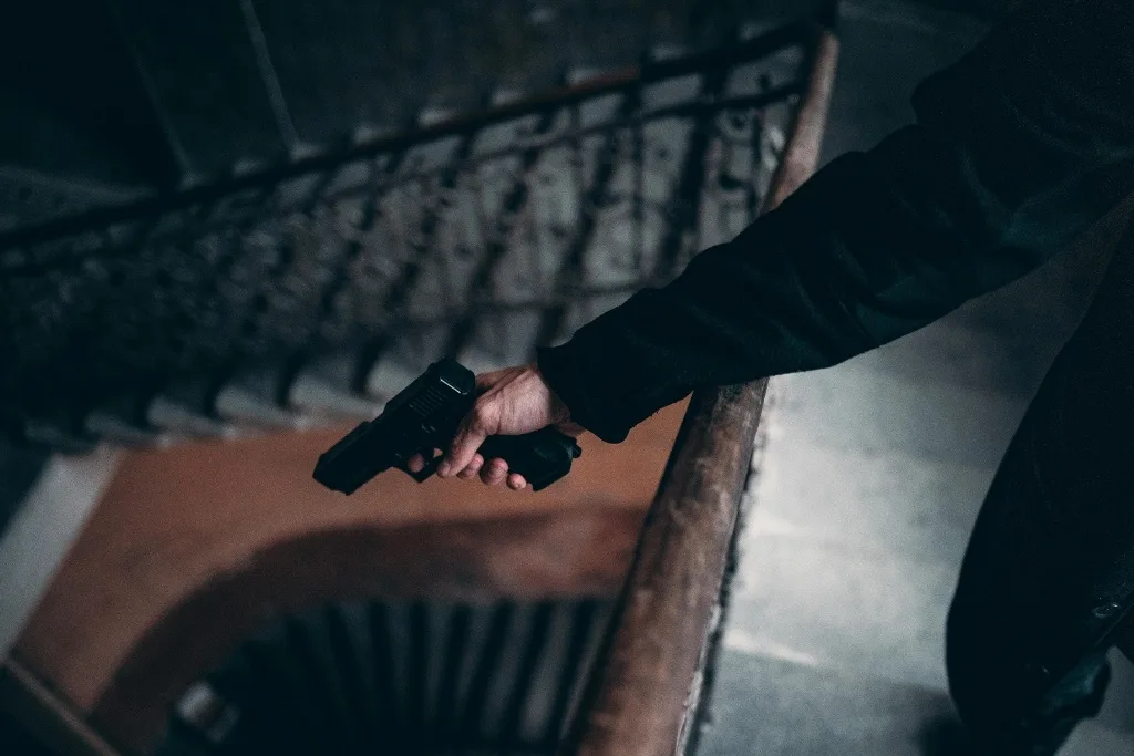 Person in dark clothing holding a handgun while descending a stairwell, emphasizing security crisis response